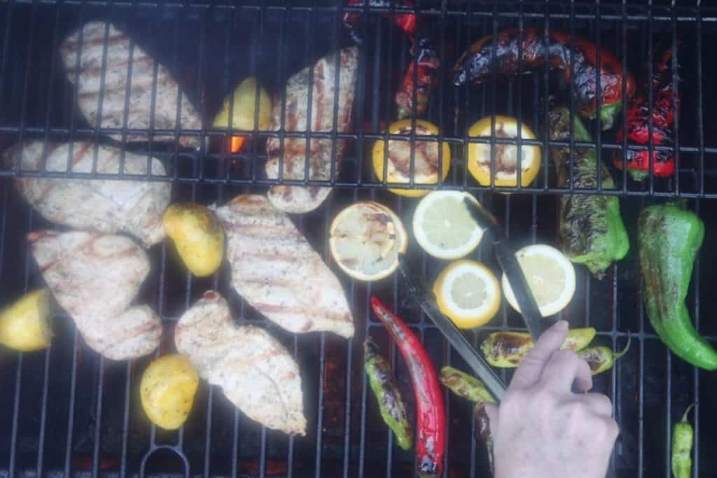 grilled lemon oregano chicken: a smoky, steamy overhead view of the chicken, lemons and peppers on the grill