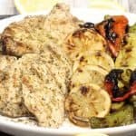 small platter of grilled lemon oregano chicken with charred lemons and clark farm peppers