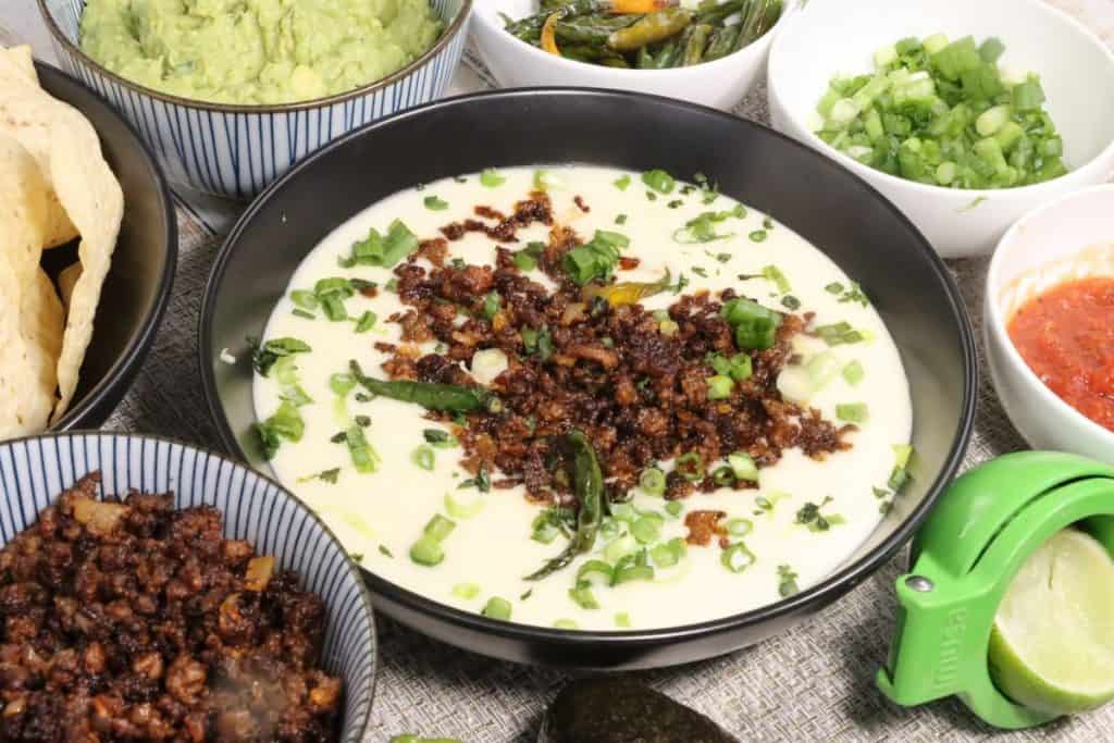 side view of super bowl white queso dip with crispy crumbled beef: put out all the fixins and everyone can serve themselves