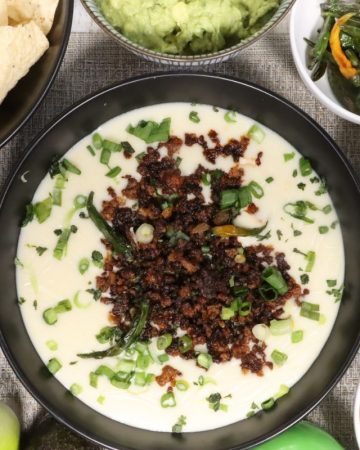 super bowl white queso dip with crispy crumbled beef: overhead view of queso dip with all the fixins including tortilla chips, crumbled beef, guacamole, chilis, scallions and salsa