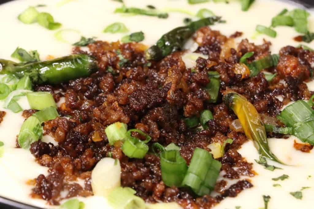 very close look at super bowl white queso dip with crispy crumbled beef. tiny spicy chilis for people who want to bring the heat
