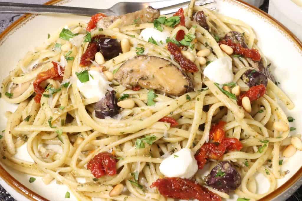 Pesto Pasta with Olives: side view close up of pasta with mushrooms, mozzarella, toasted pine nuts, sun dried tomatoes