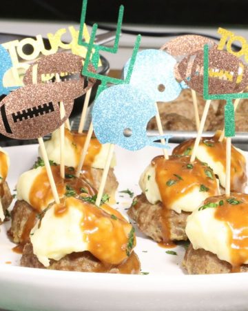 front view of super bowl meatloaf bites with mashed potatoes and gravy with extra mashed potatoes in the background and sheet pan with mini meat loaves