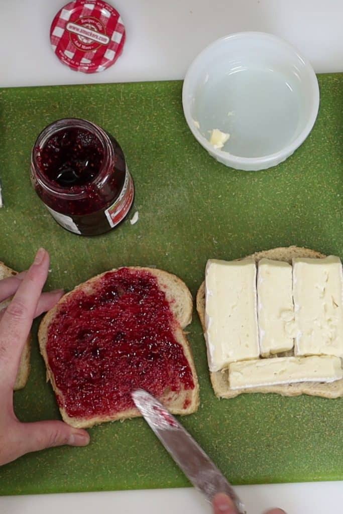 spreading the raspberry preserves on a slice of bread while assembling the sandwich