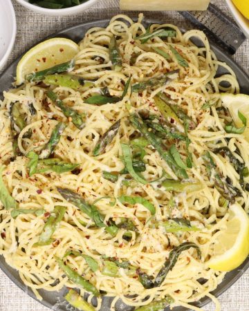 lemony spaghetti with asparagus and basil: overhead view of pasta on a serving plate with chili flakes, cheese grater and lemons in the background