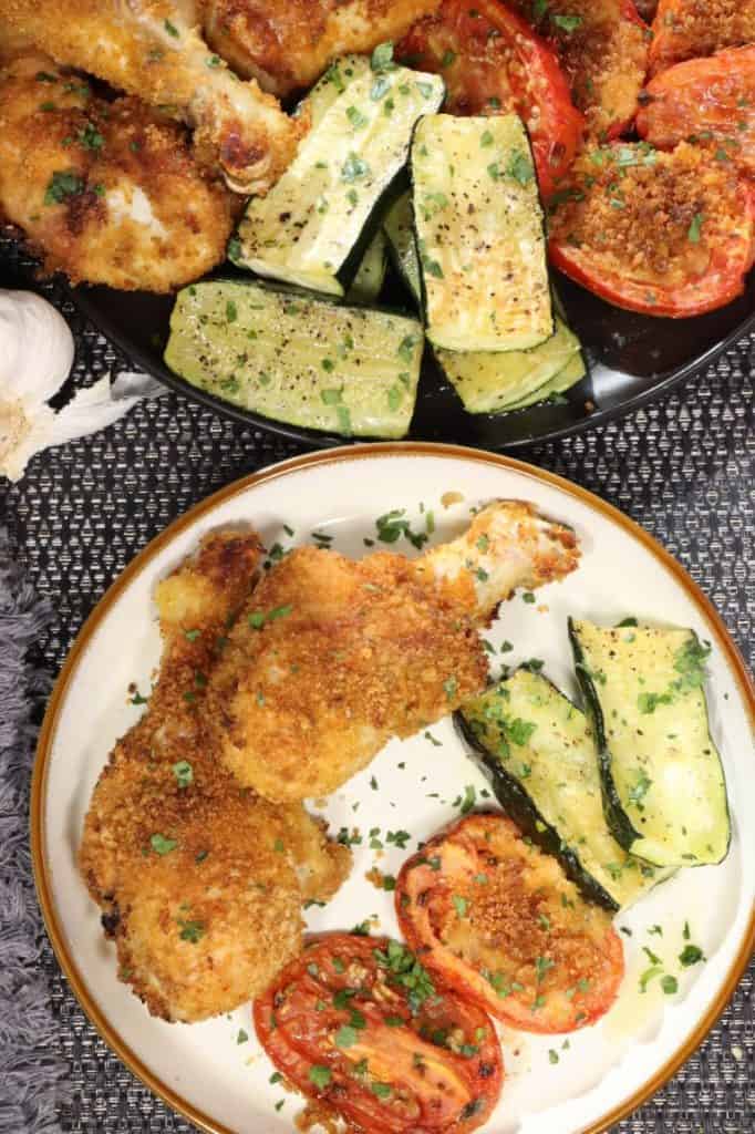 one plate with drumsticks, zucchini and tomatoes with serving platter in the background