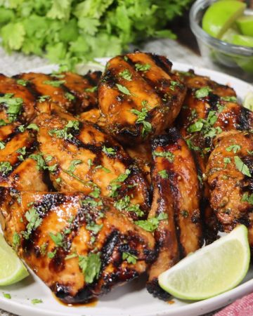 grilled sriracha lime chicken on a plate garnished with lime wedges and cilantro