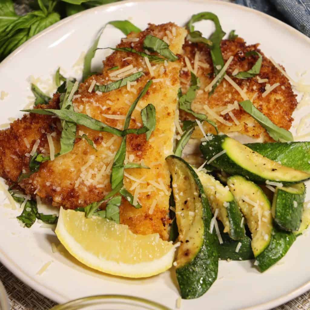 one plate with lemon butter basil chicken cutlets with parmesan cheese garnish and sauteed zucchini