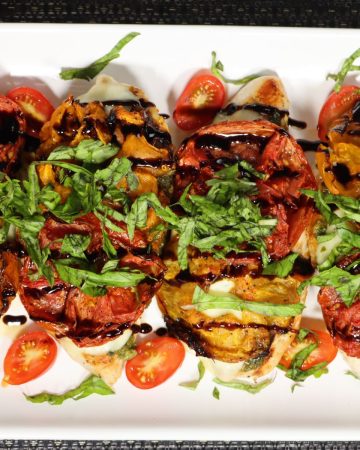 pan seared chicken caprese with roasted tomatoes and fresh basil on a serving platter with balsamic glaze