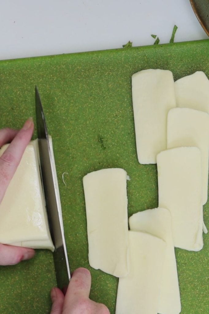slicing the mozzarella into thin pieces that will be placed on top of the chicken
