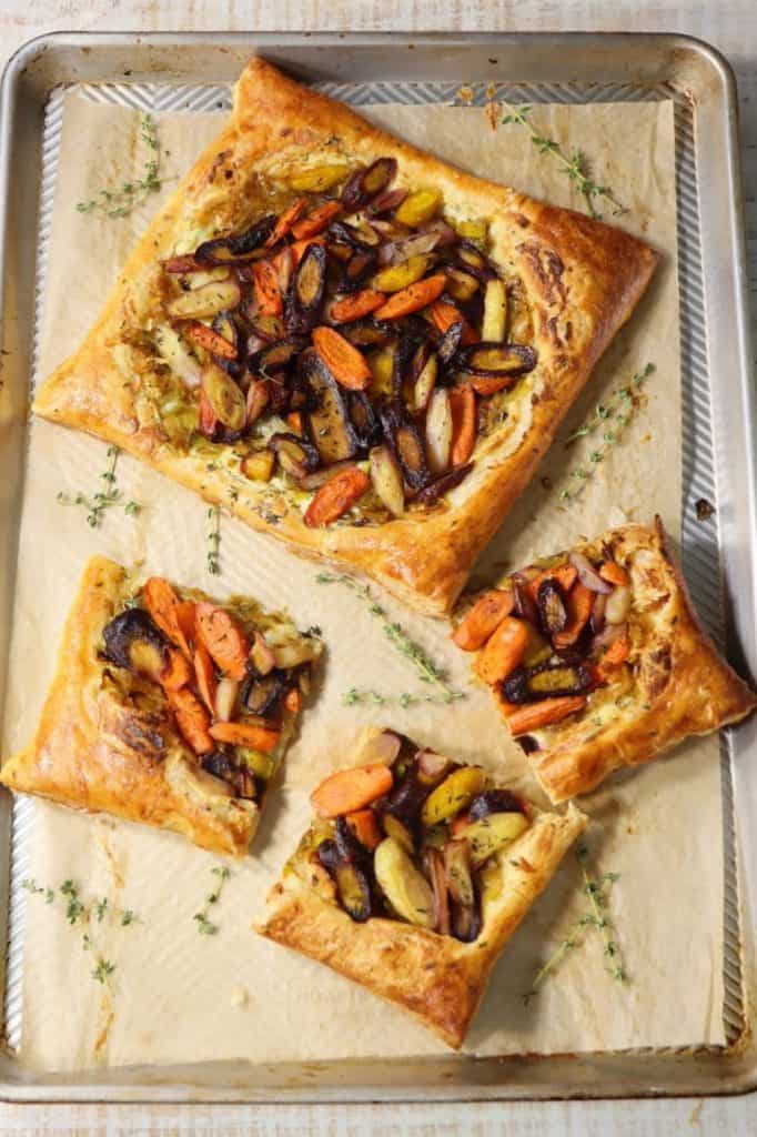 overhead view of rainbow carrot tart with leeks and boursin cheese on a large sheet pan garnished with fresh thyme sprigs