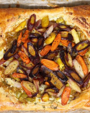 overhead view of rainbow carrot tart with leeks and boursin cheese sitting on parchment paper