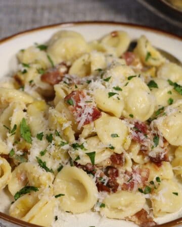 front view of orecchiette pasta with leeks and bacon garnished with parsley