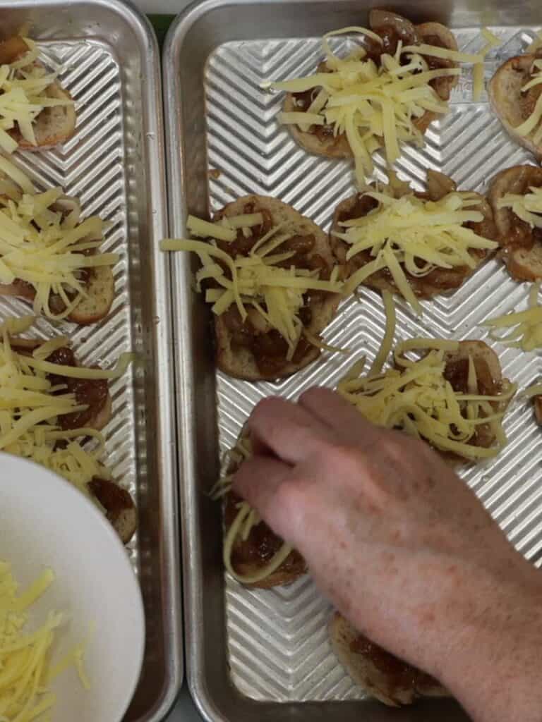 adding a pinch of gruyere cheese to the tops of french onion crostini