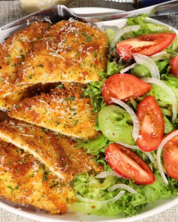 overhead view of cheddar chicken cutlets with salad in a platter garnished with pepper flakes and parmesan cheese