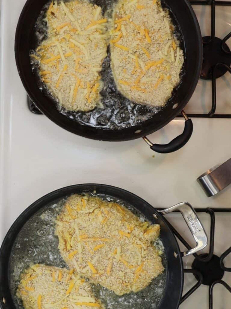 overhead view of frying cheddar chicken cutlets in two pans