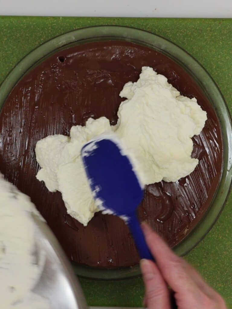 adding the whipped cream to the top of the chocolate cream pie