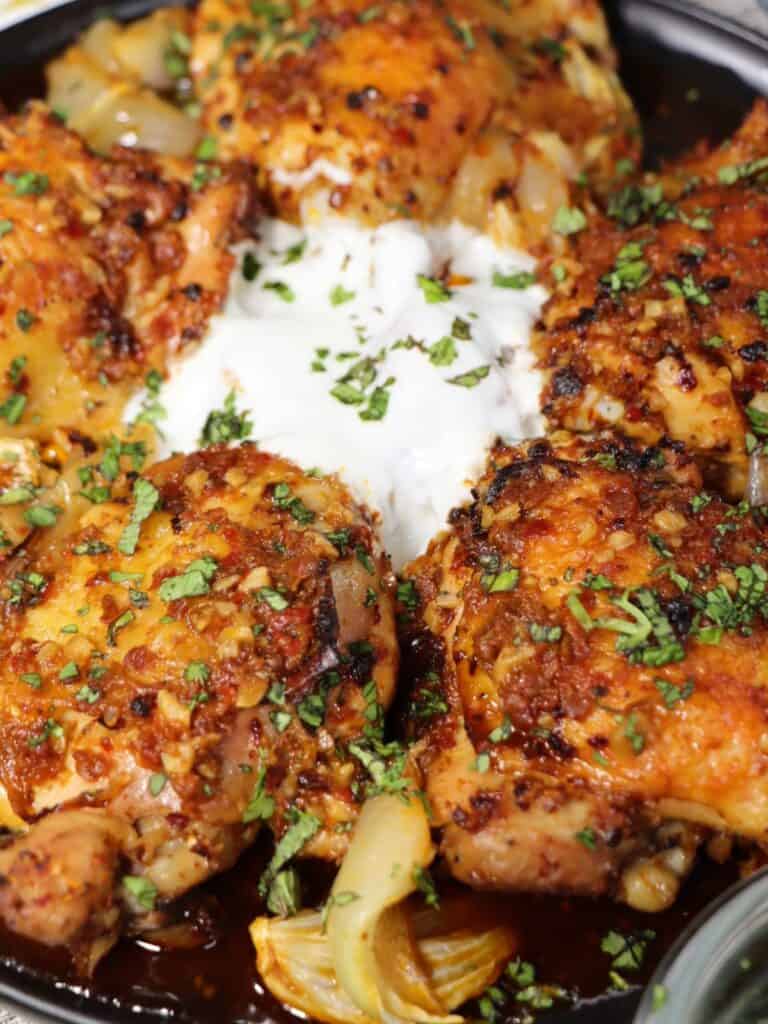 close up view of harissa chicken thighs with yogurt cilantro mint on a plate and ready to serve