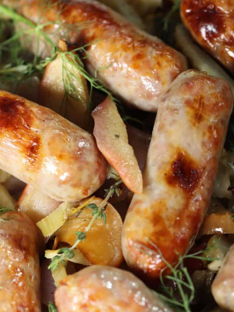 close up look at browned italian sausage on a serving plate with apples fennel and onion with fresh thyme and leafy fennel fronds