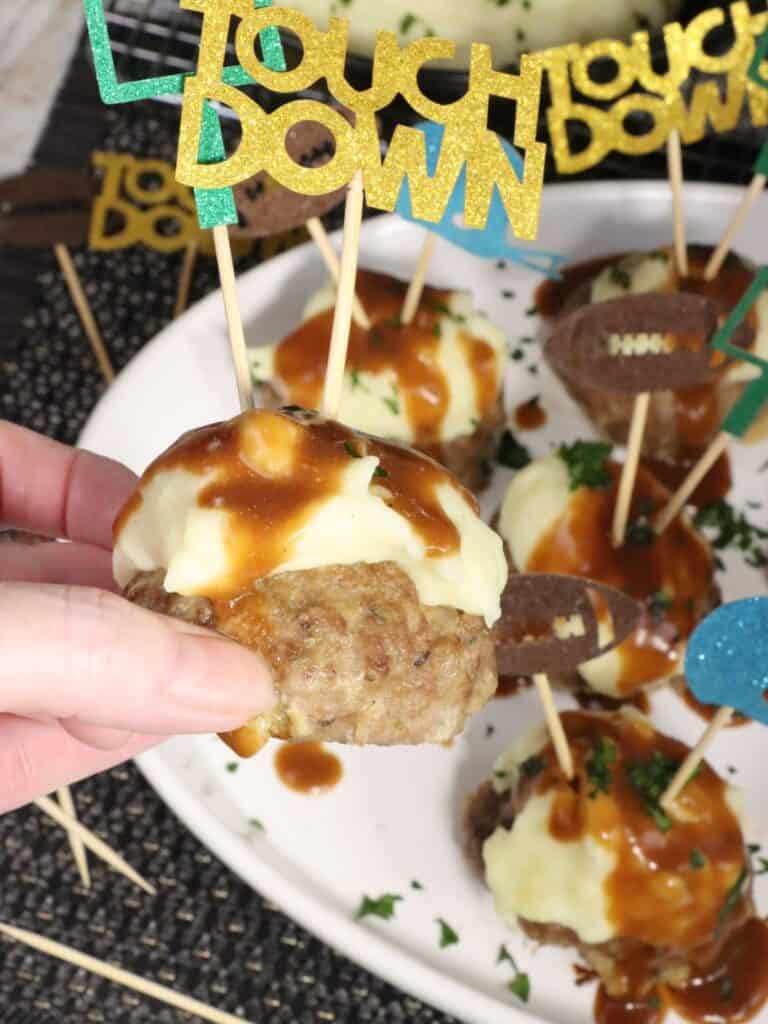close up look of one super bowl meatloaf bite with mashed potatoes and gravy and decorative football toothpicks