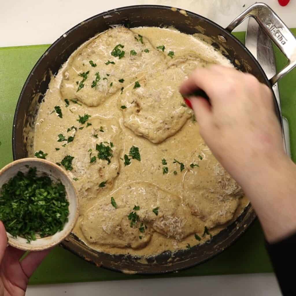 garnishing the creamy dijon chicken with cheese, parsley and lemon wedges