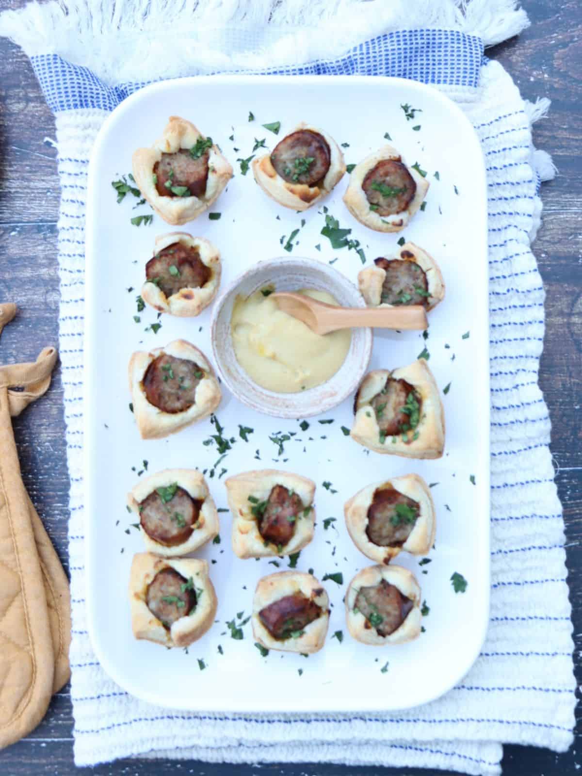 overhead view of italian sausage and dijon puffs with more dijon on the saide and a parsley garnish