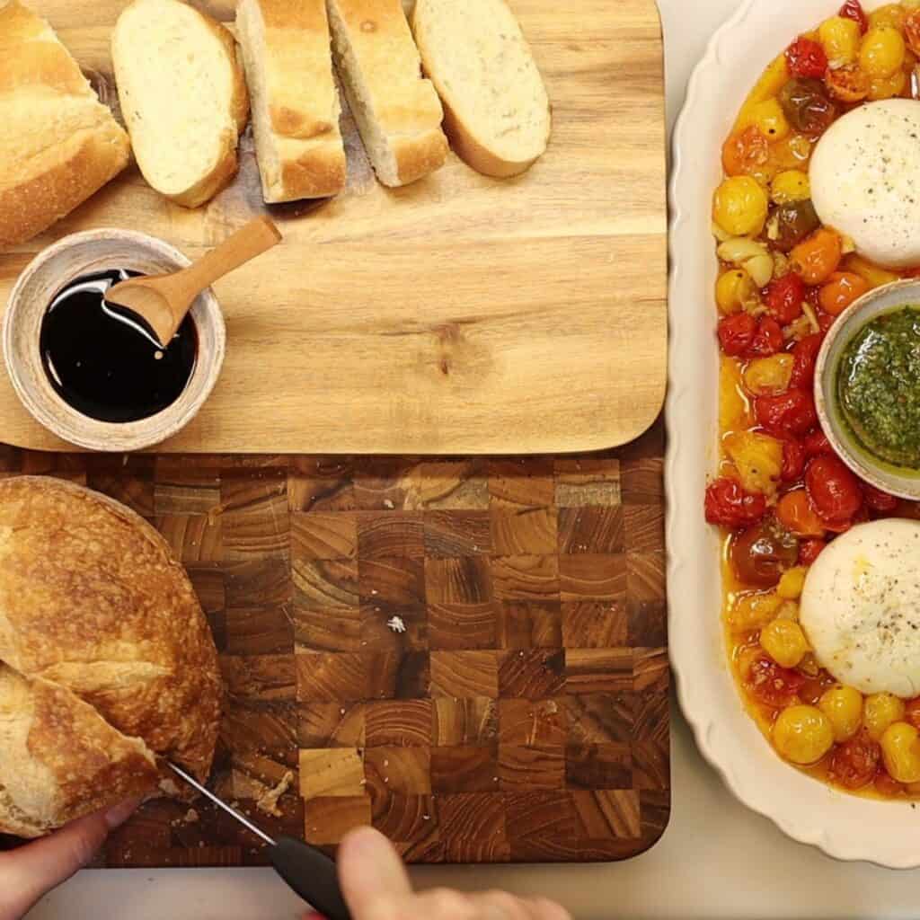 slicing bread to serve on the side of roasted cherry tomatoes with smashed garlic and burrata