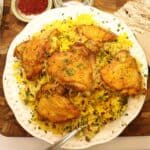 overhead view of crispy saffron chicken thighs with barberries and pigeon peas on a serving plate with saffron in the background