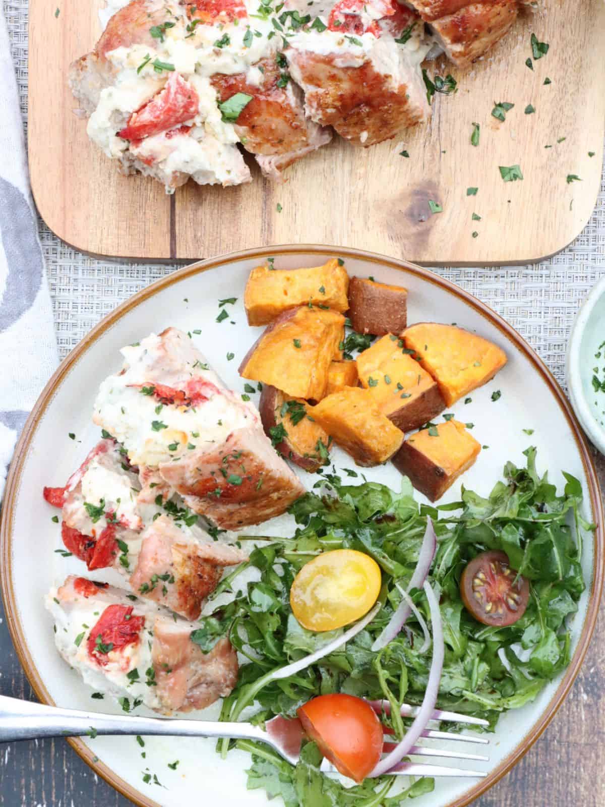 overhead view of one portion of boursin cheese stuffed pork tenderloin with sweet potatoes and arugula