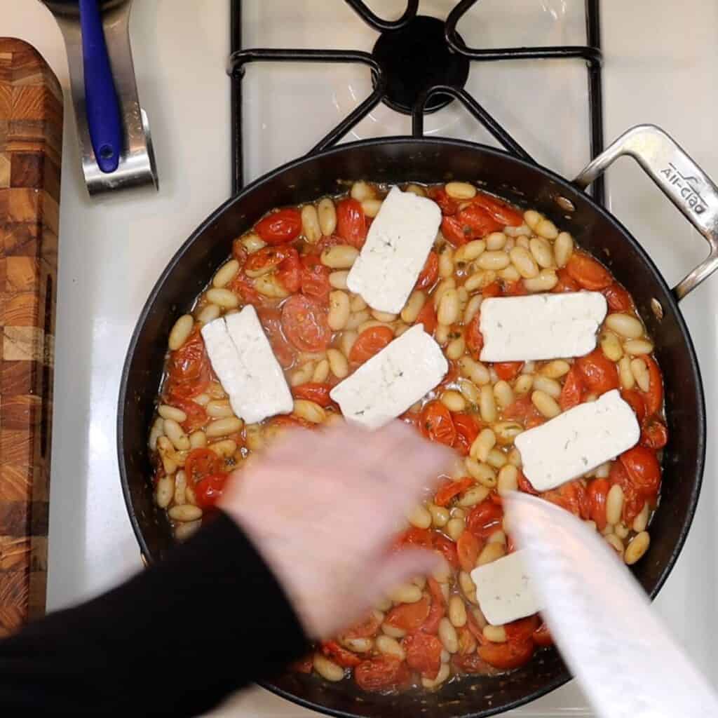 placing sliced halloumi cheese on tomatoes and white beans before broiling to crisp