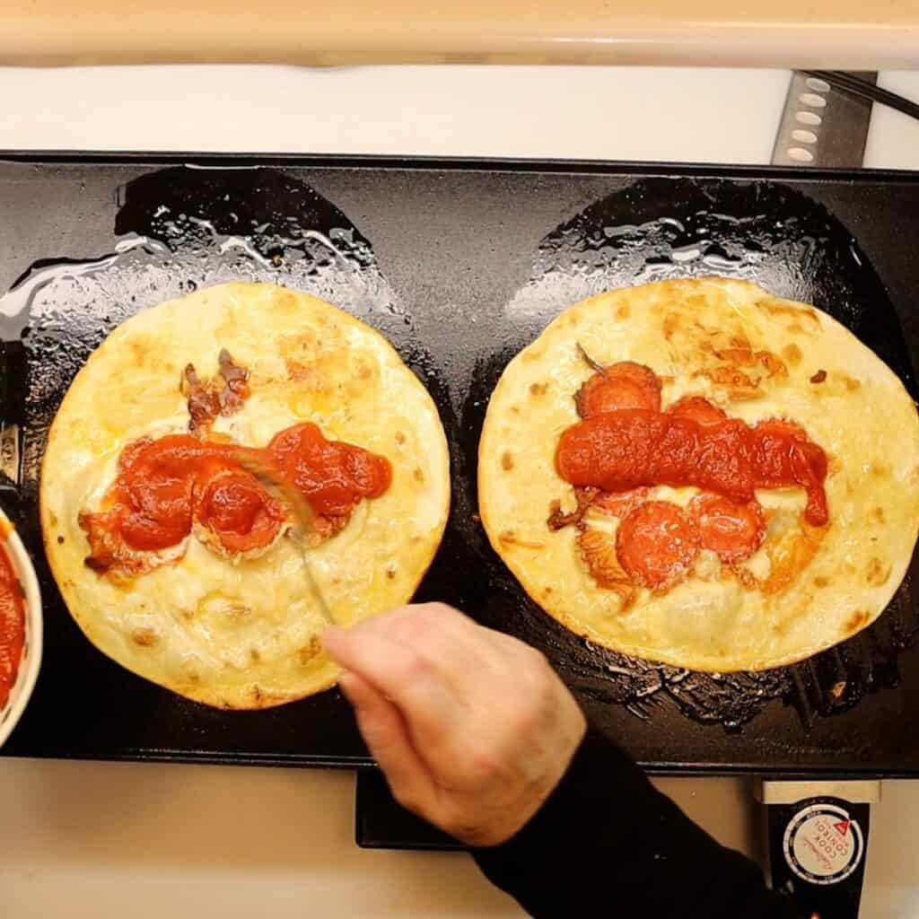 spooning marinara sauce onto pepperoni pizza roll-ups