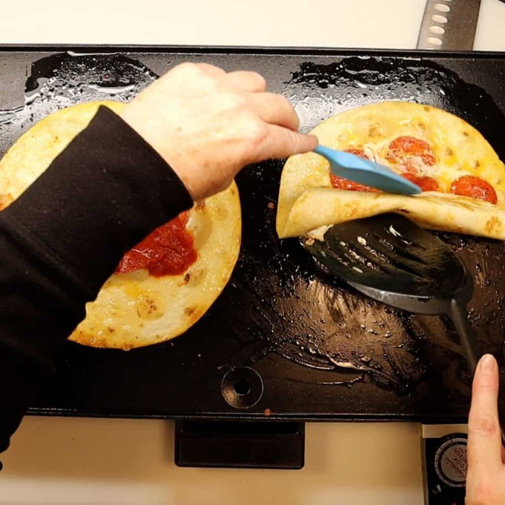 using two spatulas to roll the pepperoni pizza roll-ups