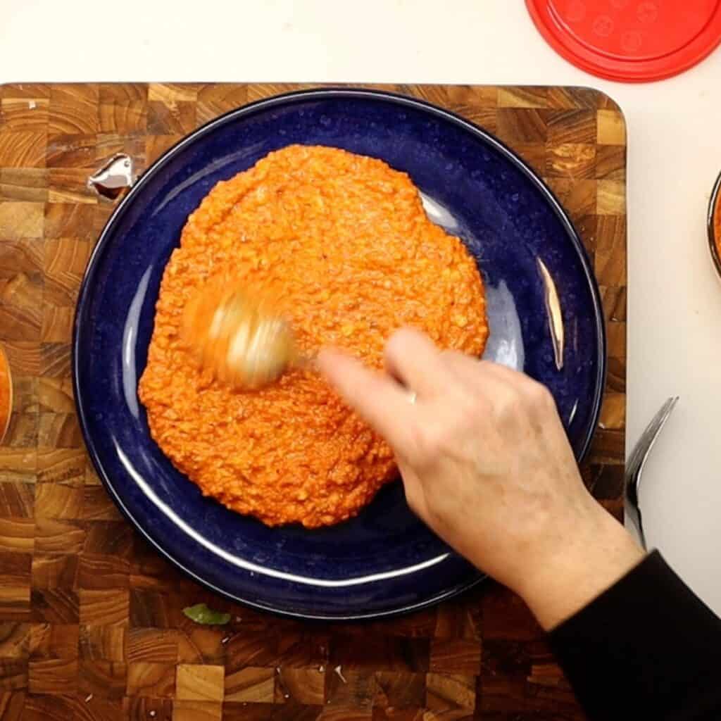 spreading blended romesco sauce onto a serving plate for roasted cauliflower with romesco sauce