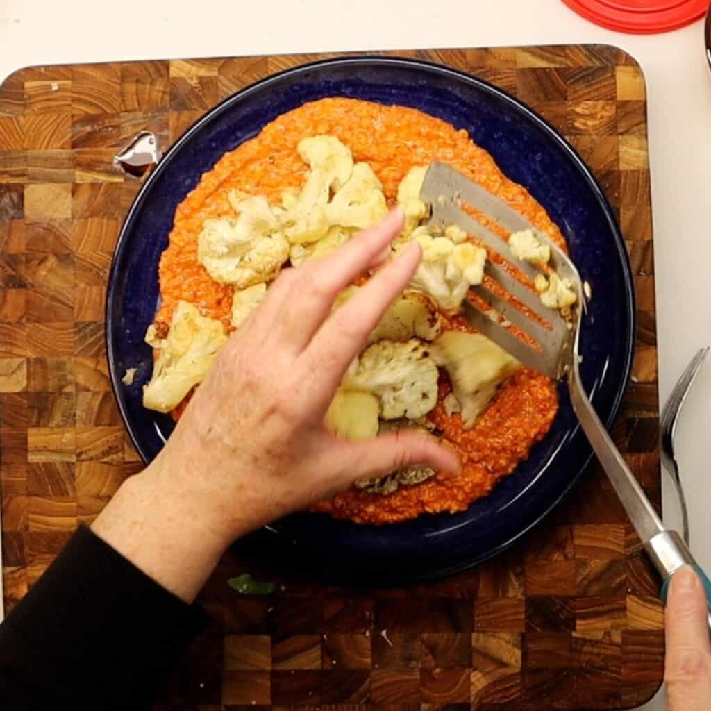 adding roasted cauliflower on top of romesco sauce