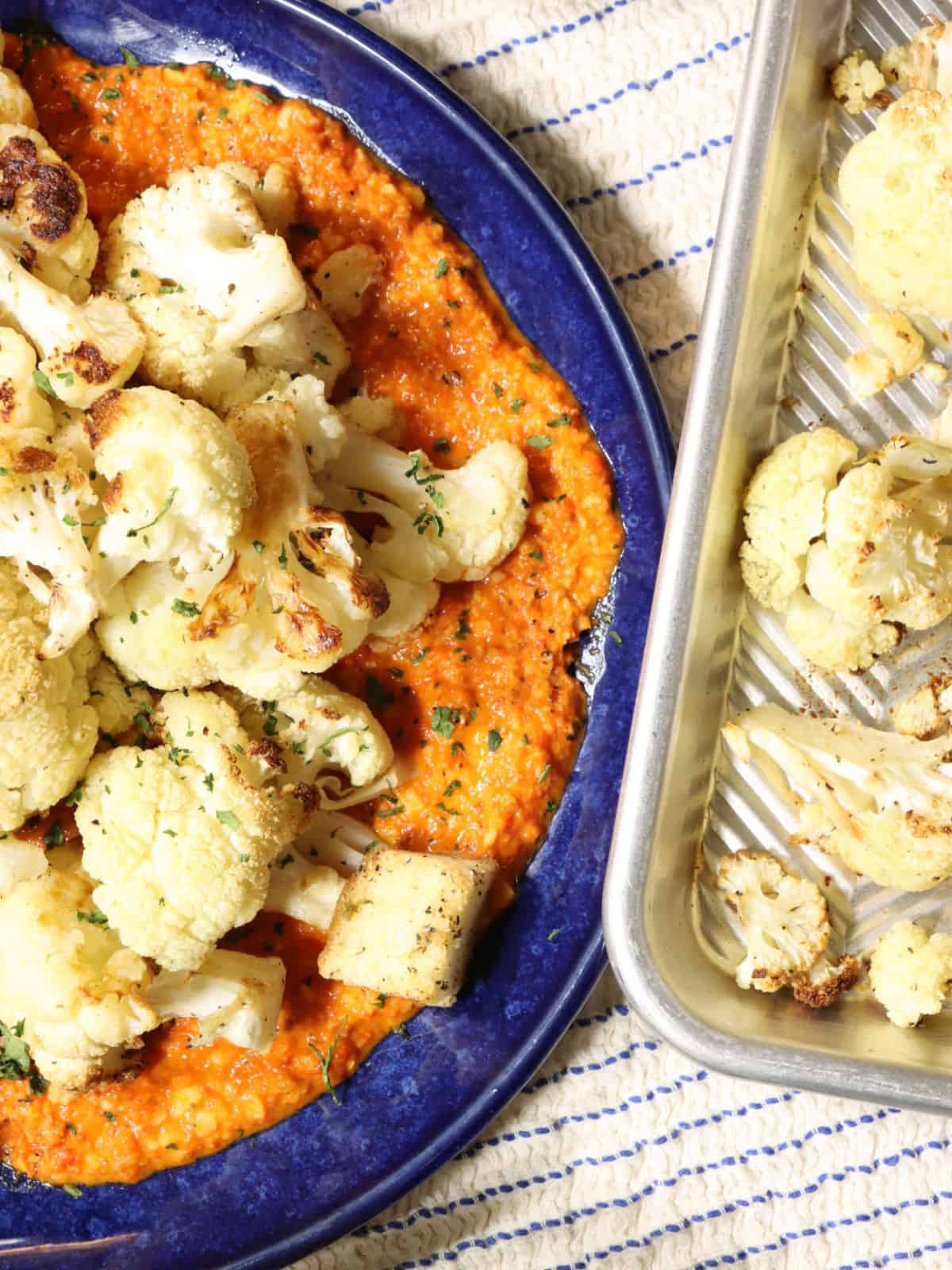 roasted cauliflower over romesco sauce on a plate next to sheet pan with cauliflower