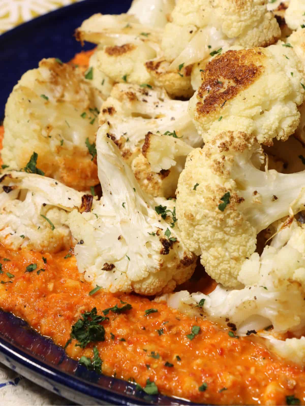 close up look at roasted cauliflower with romesco sauce on a serving plate