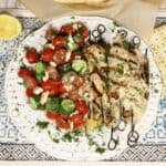 grilled za'atar lemon chicken skewers on a plate with tomato, cucumber, salad