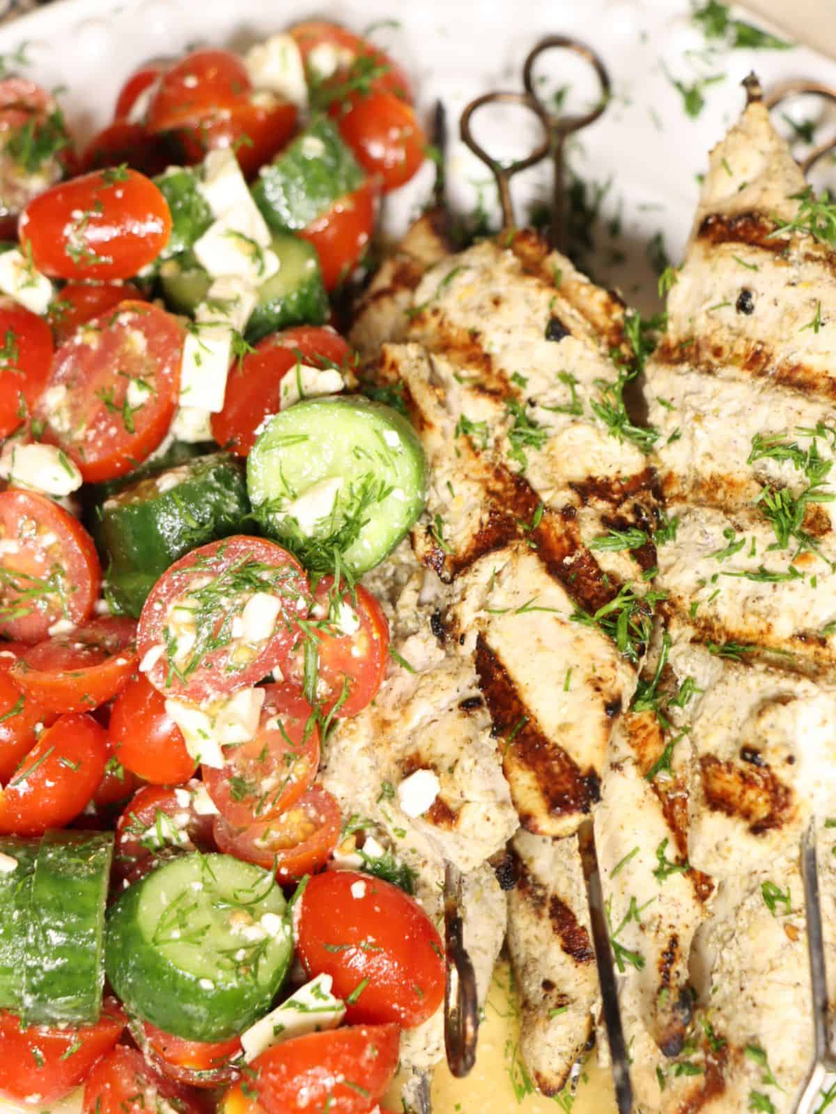 overhead view close up of grilled za'atar lemon chicken skewers on a plate with tomato, cucumber, salad